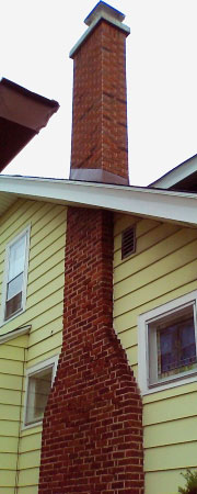 Brick chimney on side of yellow house with finished Tuckpointing repairs, new crown and caps