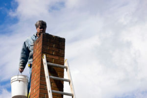 man with bucket climbing ladder next to chimney on roof
